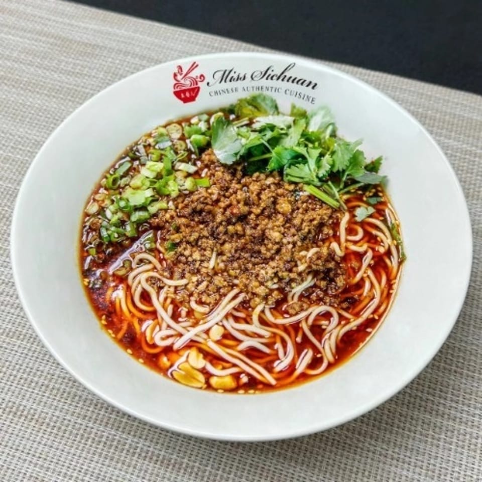 A bowl of Miss Sichuan dan dan noodles with minced pork, chili oil, peanuts, and cilantro.
