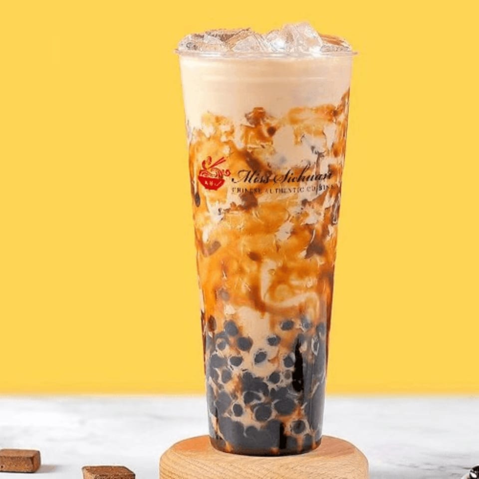 A Miss Sichuan brown sugar boba milk tea with ice, against a yellow background.